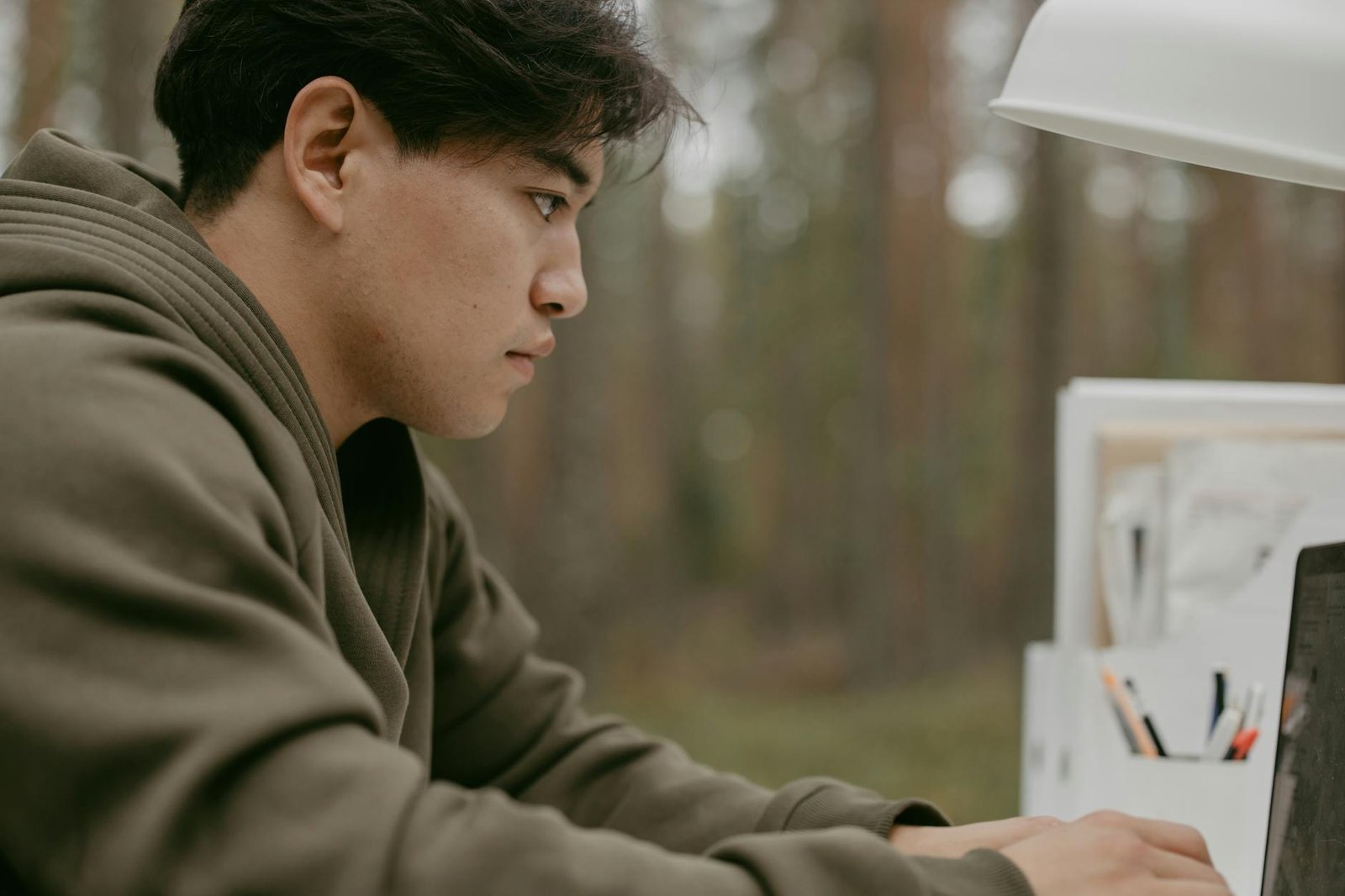 Young man in a green jacket using a laptop outdoors, concentrating on his work.